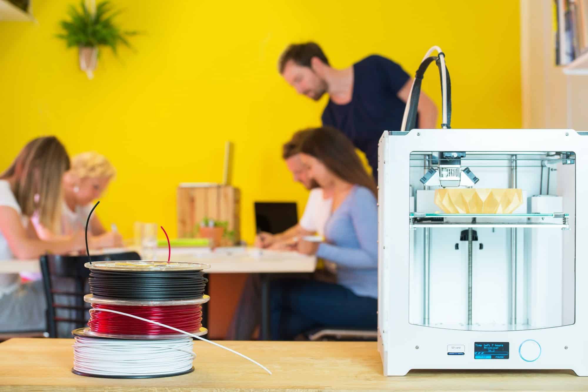 Impresora 3D con diseñadores en segundo plano